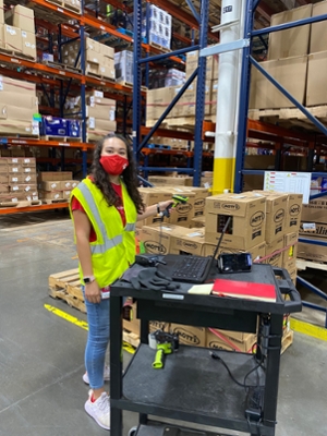 Photo of Kaylee at work in the Target distribution center. She is wearing a red face mask and a high-visibility vest and holding a scanner.