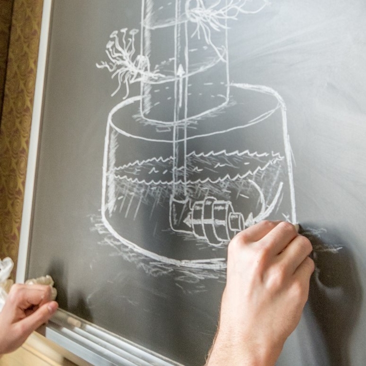 hands sketching rotary pump on chalkboard.