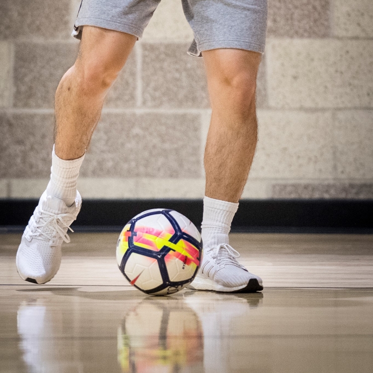 man's legs kicking futsal ball in indoor gym.