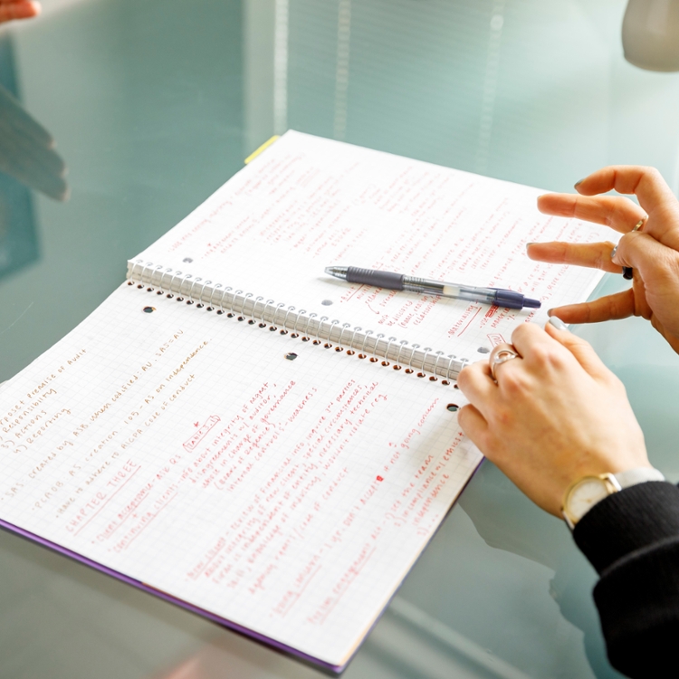 hands gesturing over spiral notebook open on glass table.