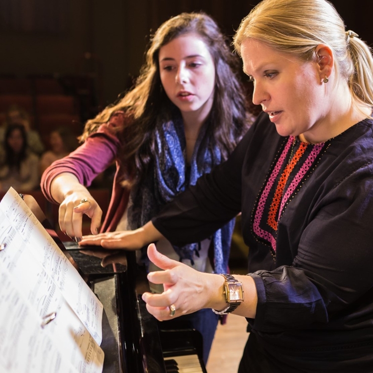 Student Catherine Jacobs and professor Nicole Hanig talking about a song in a ringed binder on a piano.