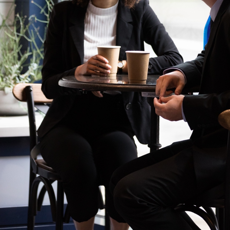 two people sitting at table with disposable coffee cups.