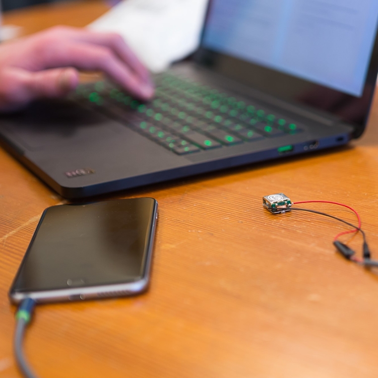 hand on open laptop keyboard with smart phone and wired chip nearby.