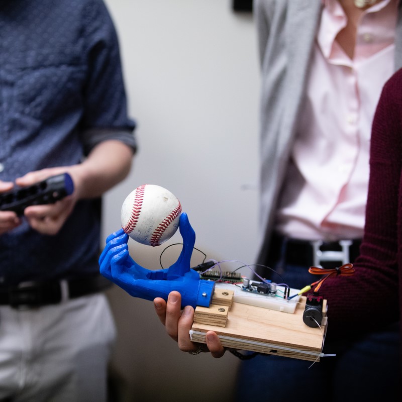 student's hands holding artificial blue hand holding baseball