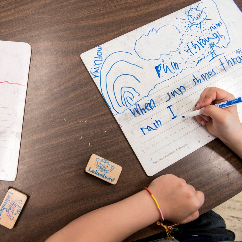 child's hands writing on small tabletop whiteboard