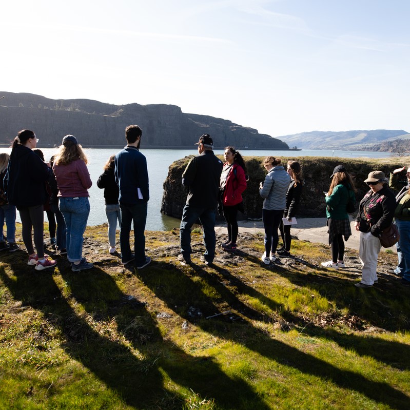 group of people outside on short cliff overlooking river