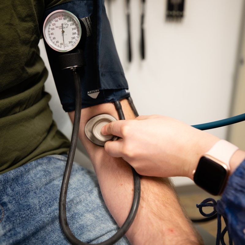 arm in blood pressure cuff with another person's hand putting a stethoscope to the cubital fossa