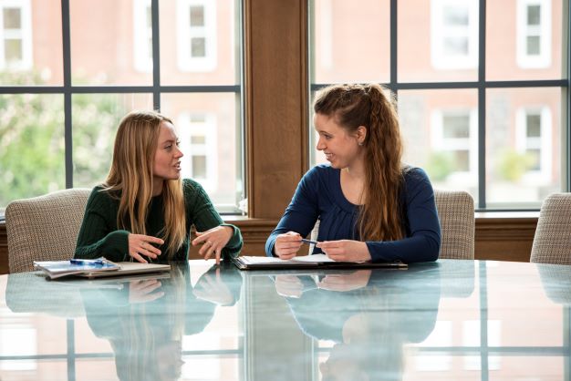 student talking with staff member in front of large window background