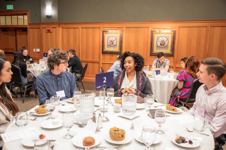 Guest speaker sitting at round dinner table with undergraduate students in the President's board room