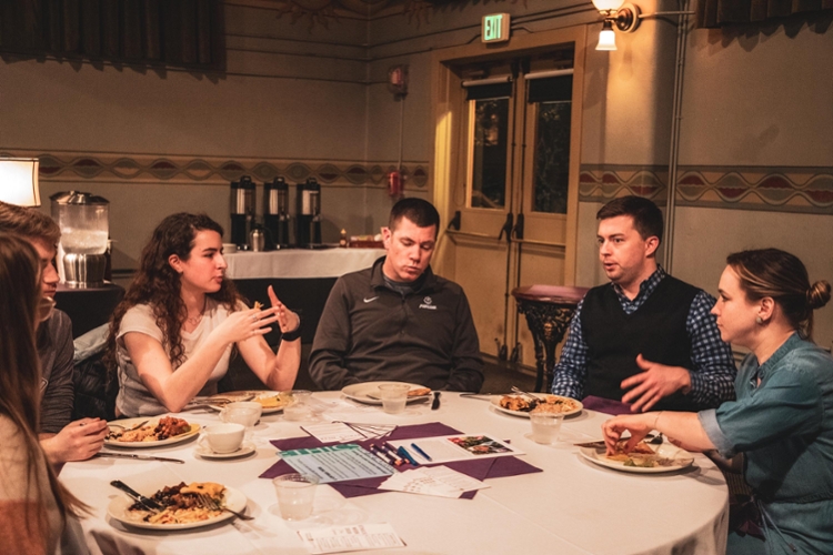 students and staff conversing at table while eating