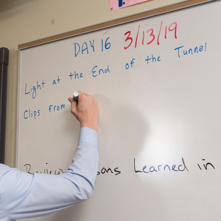 arm in dress shirt writes on whiteboard.