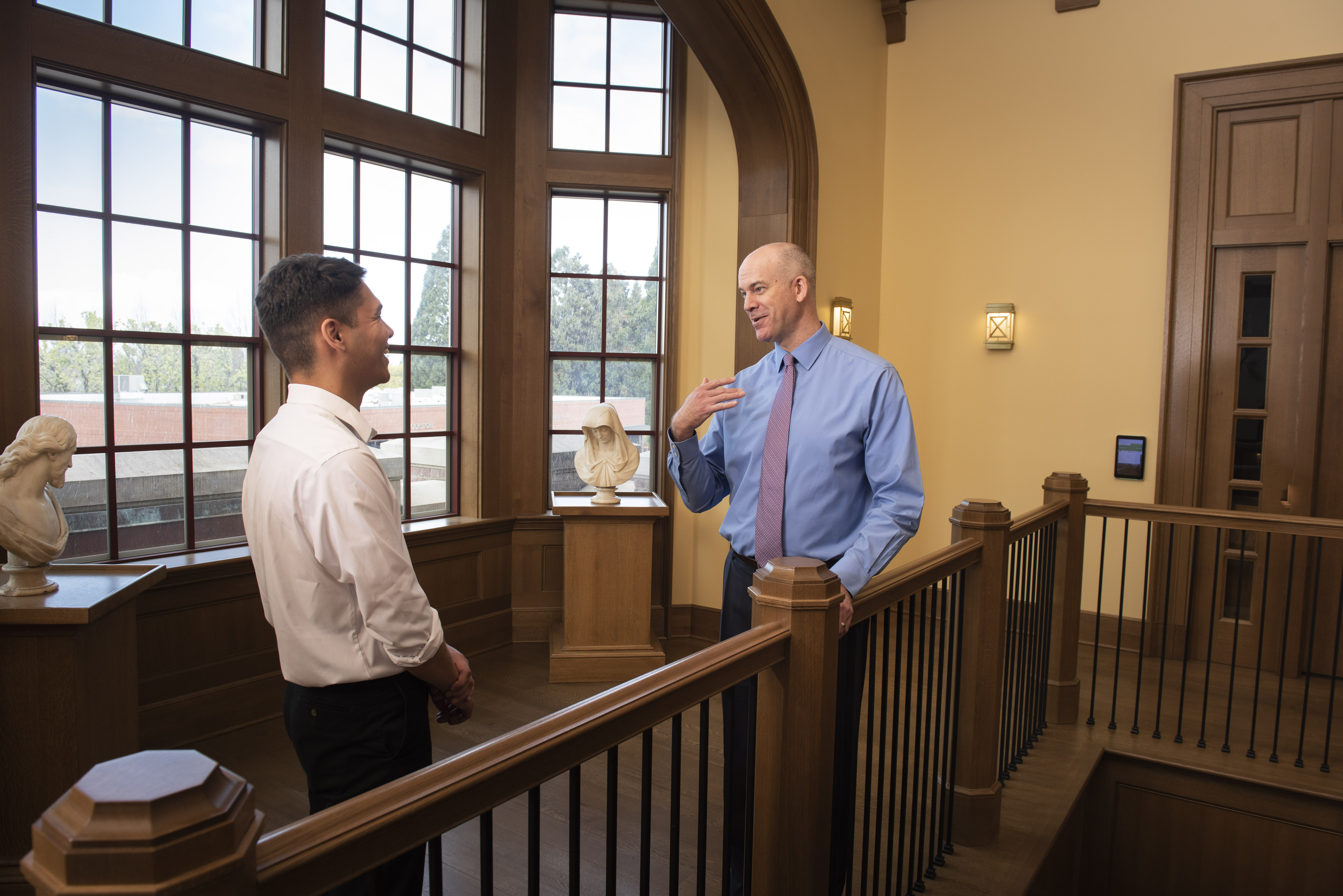 student talking with staff member near large windows