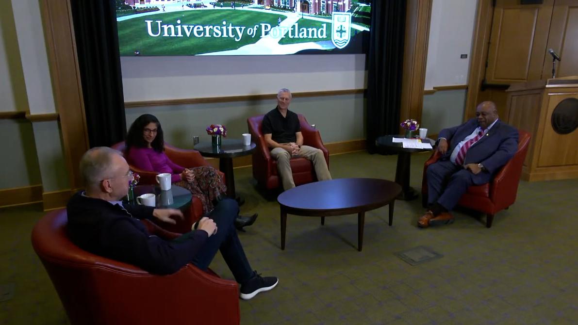 four people sitting in semicircle of low red armchairs with University of Portland screen in background