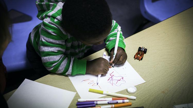 child in green hoodie coloring with thin markers