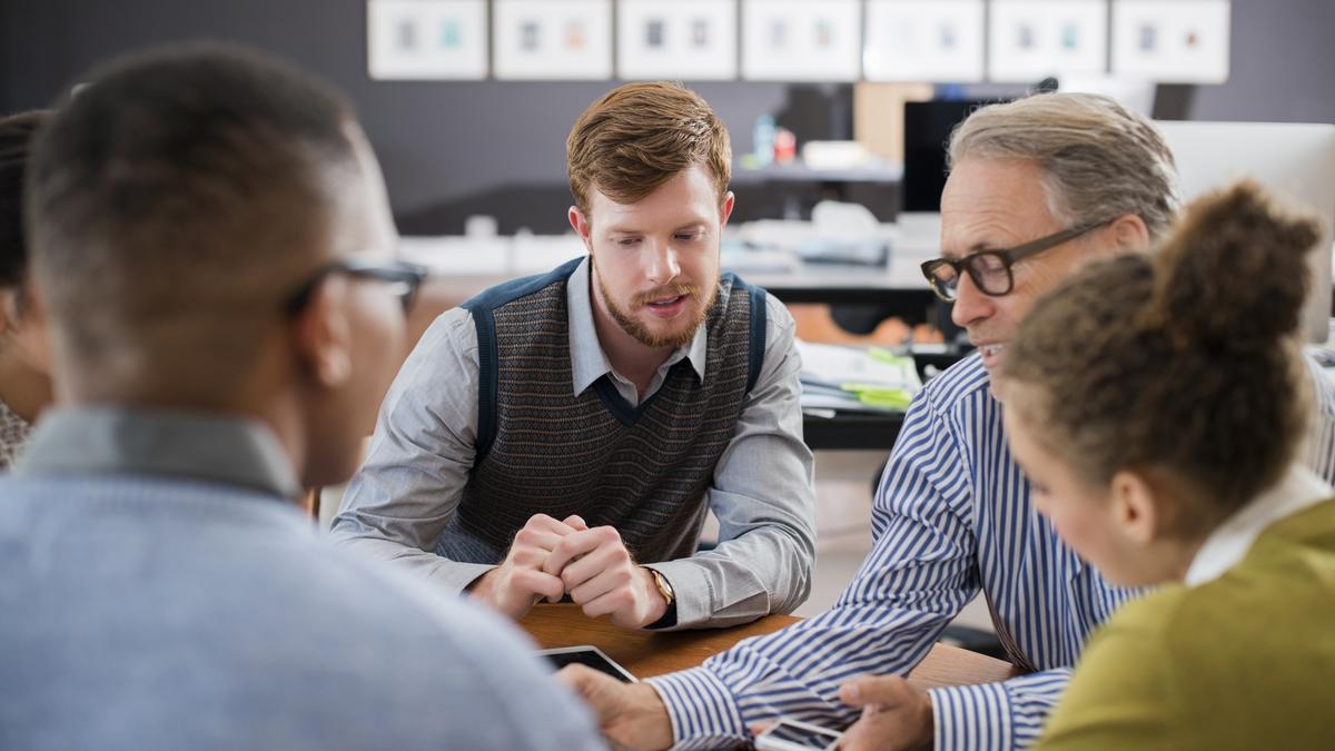 group of young adults sitting at table talking with older adult over paperwork