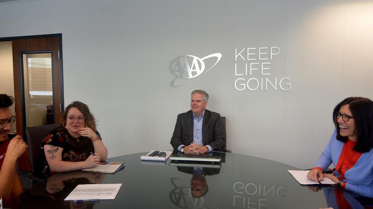 Tim Morgan sitting at table near AAA logo on wall, talking with colleagues