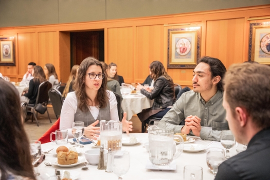 students at dinner table listening to female guest speaker seated with them