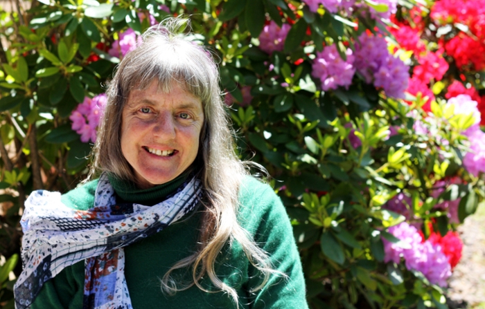 Disability rights activist Susan Sygall sitting in wheelchair in front of large green bush