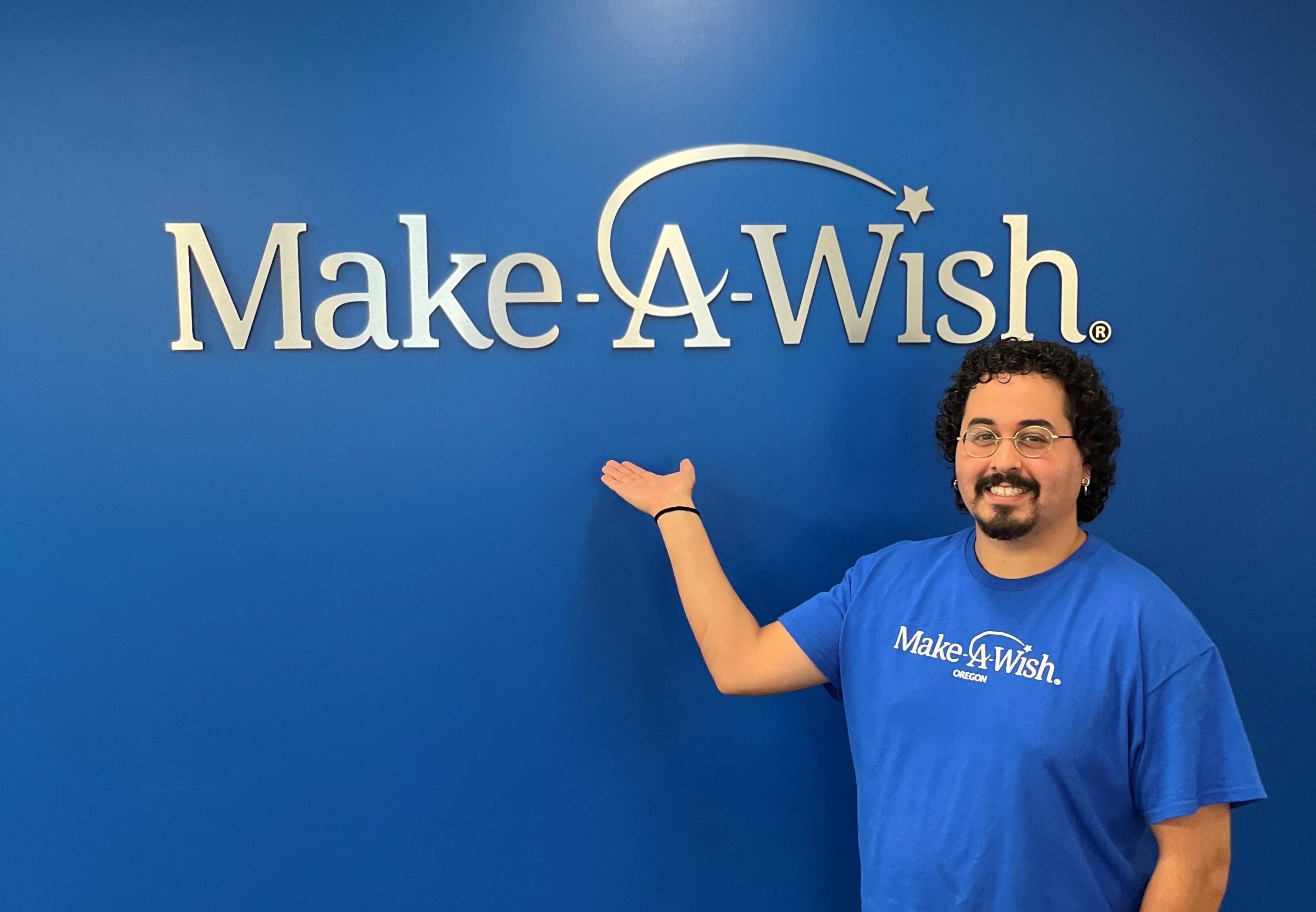 student David Montanez in blue Make-A-Wish shirt posing by blue Make-A-Wish wall