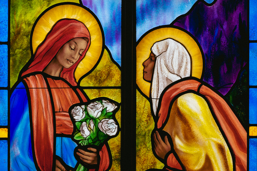 A colorful stained glass window in Sacred Heart Chapel depicting two robed figures, one holding a bouquet of roses.