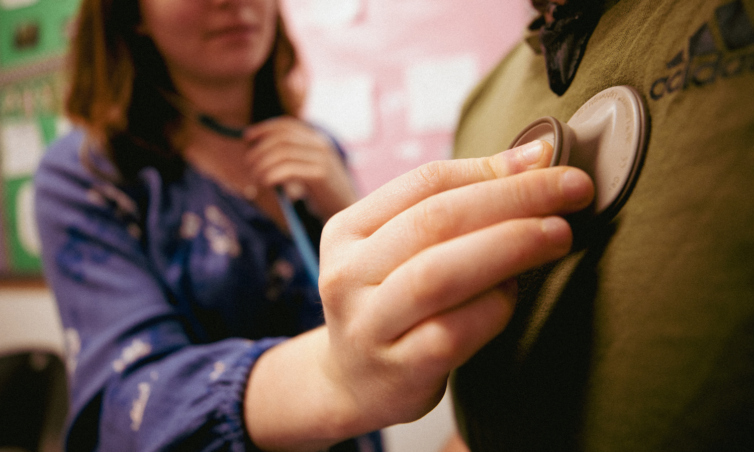 A close-up of a student using a stethoscope to listen to the chest of another person while volunteering at Blanchet House.