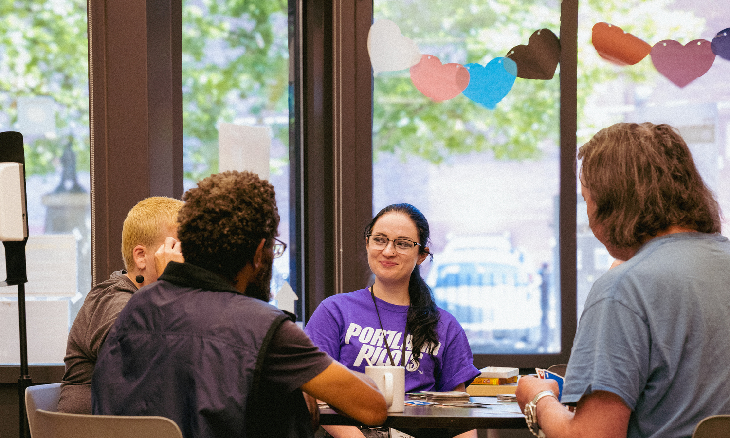 Four students sit around a table and talk in the Maybelle Center, with one student wearing a shirt that says "Portland Pilots."