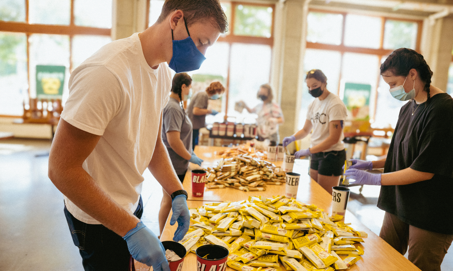 A group of students wearing gloves and masks sorts supplies at a table as part of a community outreach event.