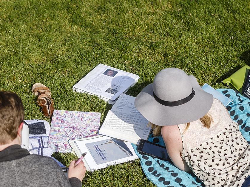 Two students take a relaxing study break in the grass on a sunny day