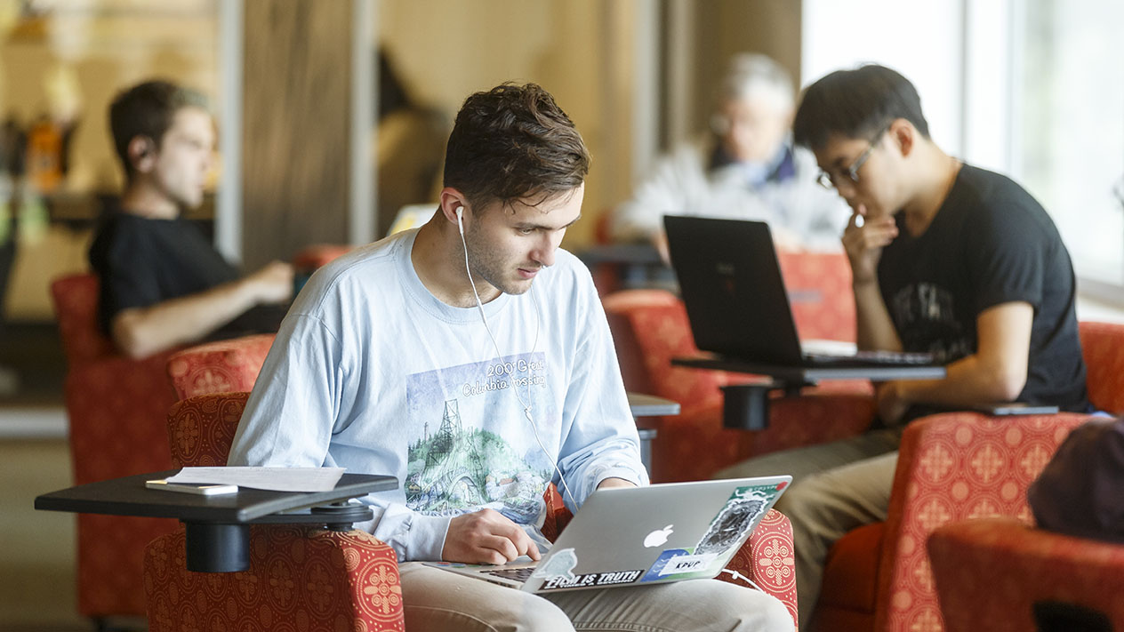 A student wearing headphones and sitting alone, looking at their laptop