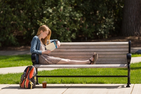 a student sits on a bench reading a book in the sunshine