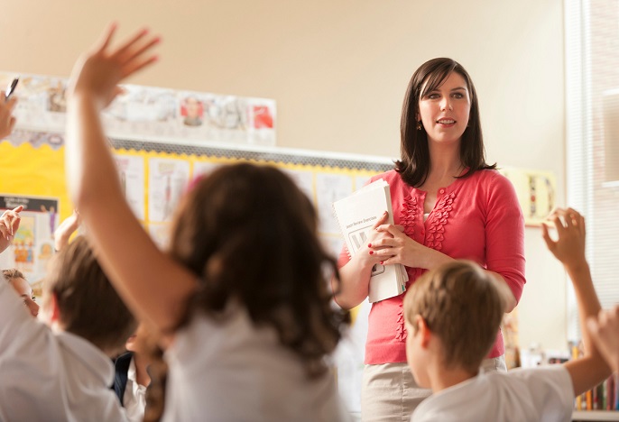 teacher at front of the classroom with students who have their hands raised 