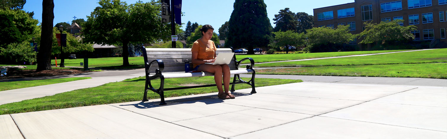 student working on a laptop on a bench outside.
