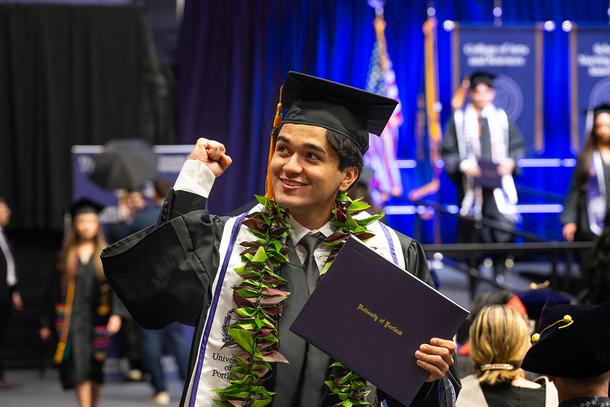 graduating student holding diploma pumps fist after crossing the stage
