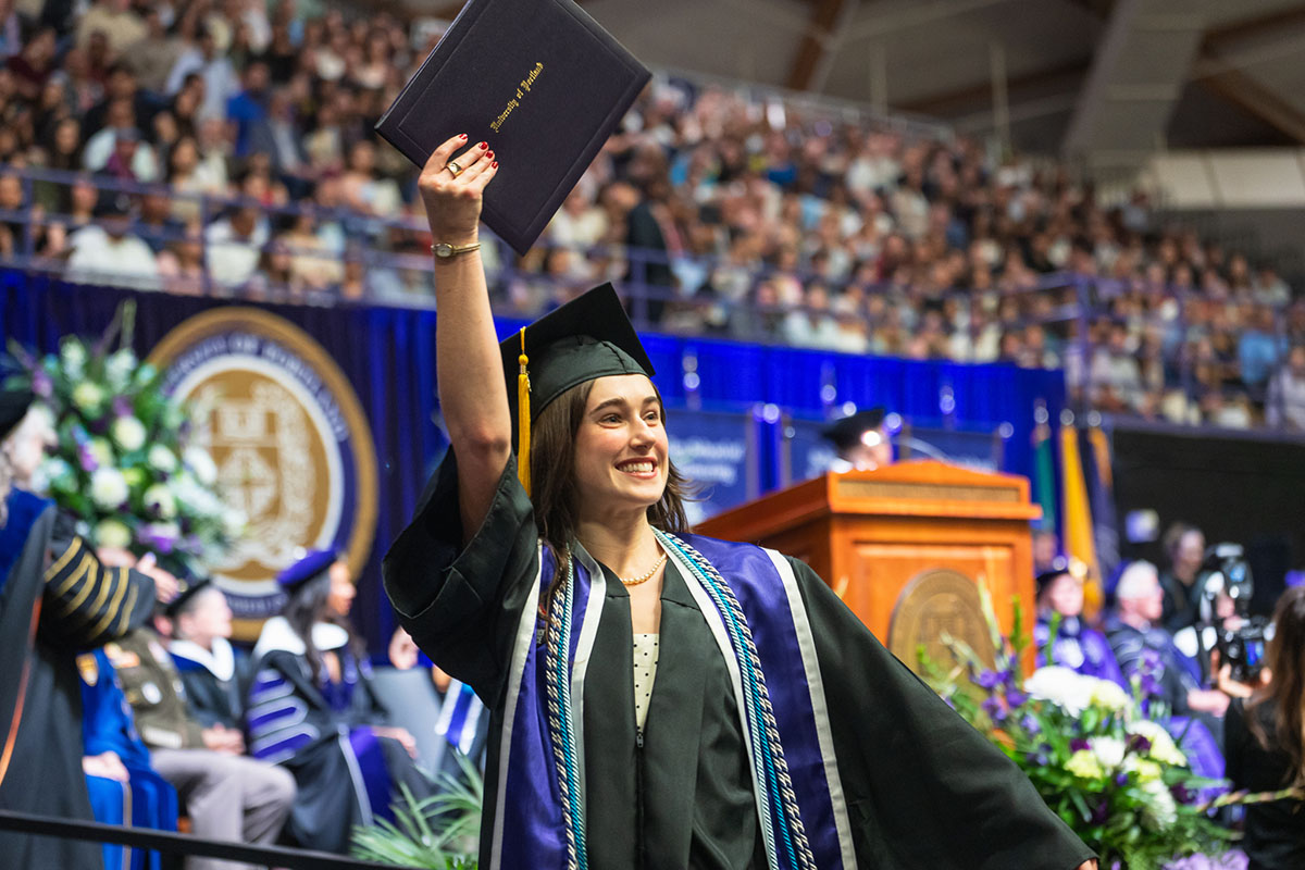 UP graduate raises her diploma up while crossing the stage at commencement