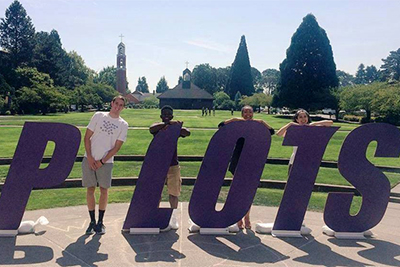 Four people standing with letters spelling Pilots