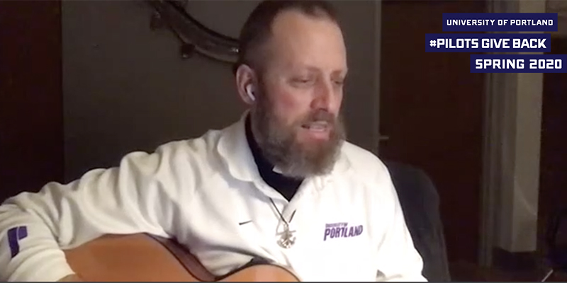 Fr. Dan Parrish holding a guitar with logo that reads University of Portland Pilots Give Back Spring 2020 