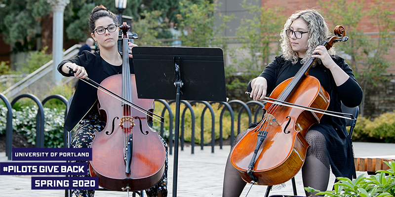 Two women playing cello with logo that says University of Portland Pilots Give Back Spring 2020