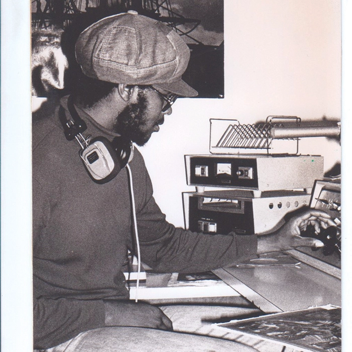 A vintage black and white photograph from 1977 man sits at the soundboard of a college radio station.