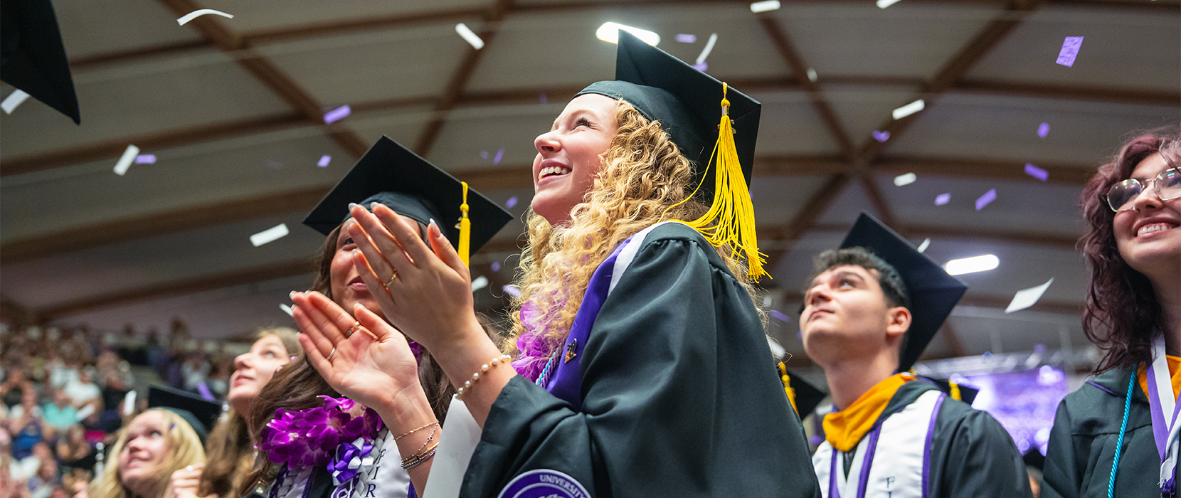 a graduate in cap and gown claps and smiles