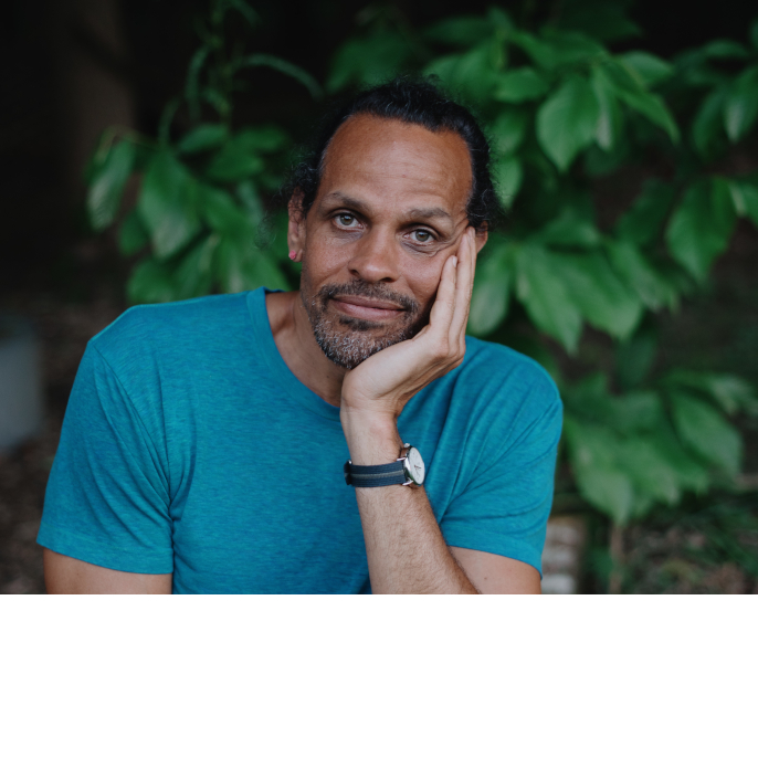 author Ross Gay in front of trees with his hand propping up his face