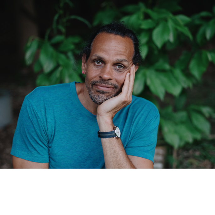 author Ross Gay in front of trees with his hand propping up his face