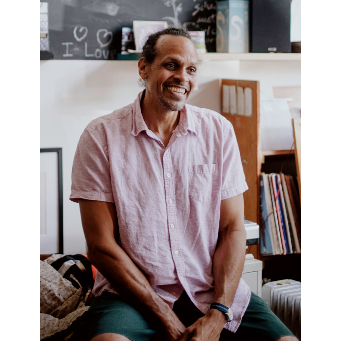 Ross Gay smiling in a room with a blackboard and vinyl records in background