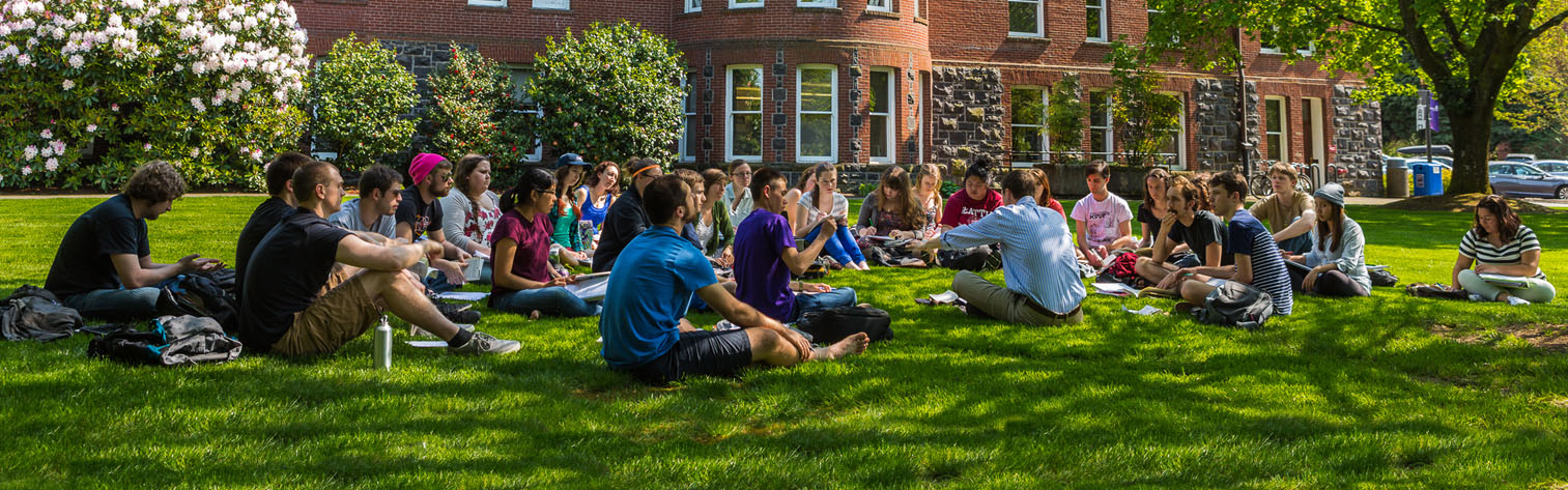 Waldschmidt Hall on sunny day with class held outside as students sit in grass with professor
