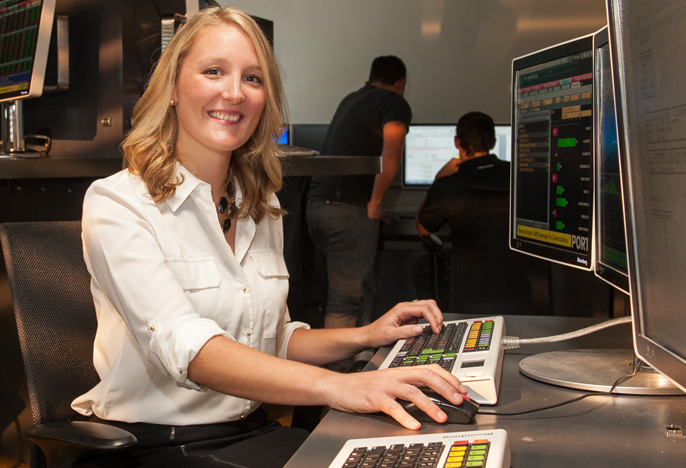 woman in white shirt sitting at desk typing on desktop computer, smiling