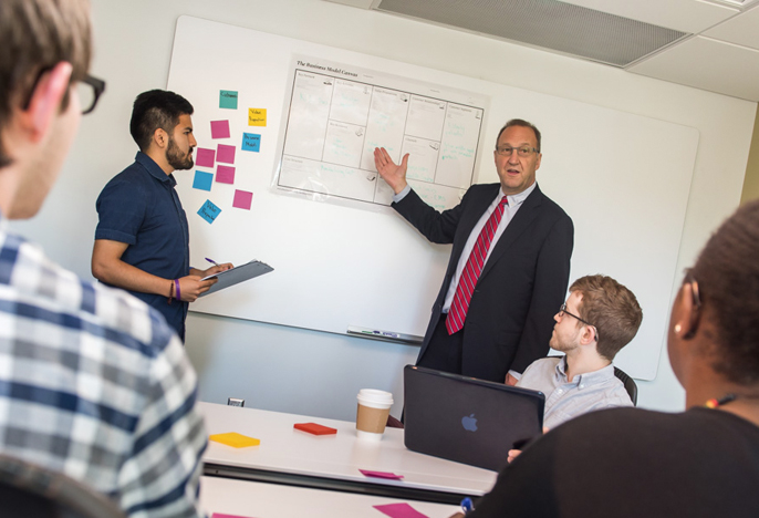 students in classroom watching a presentation given by a professor. 