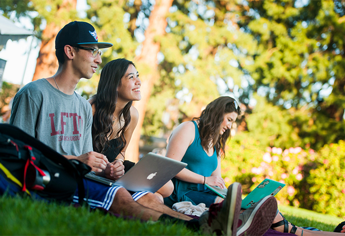 Students with computers sitting outside 