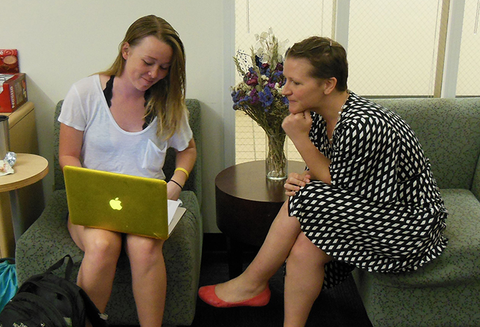 student and staff member sitting on chairs in an office, both looking over a laptop. 