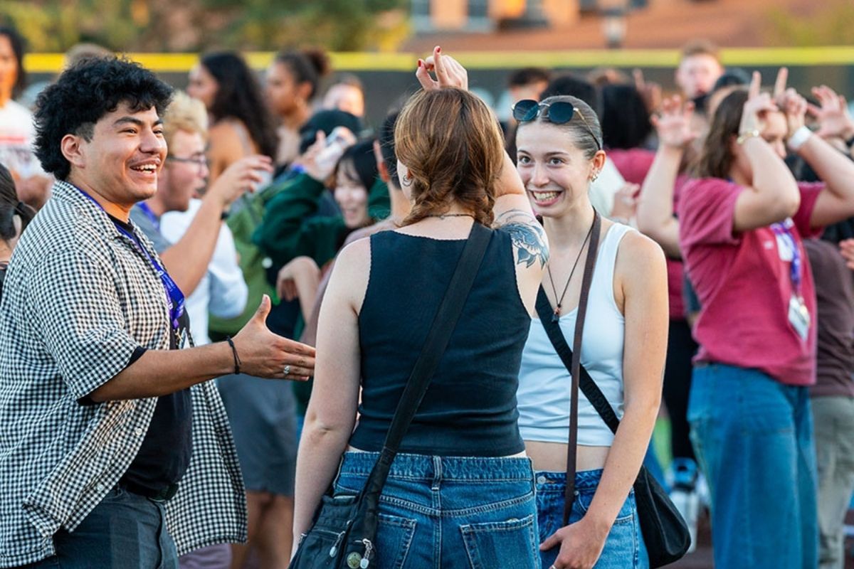 A group of students outdoors at a campus event, smiling and cheering while talking and raising hands at UP Orientation.