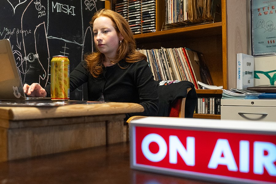 A student behind the kdup radio desk with an "on air" light in the foreground