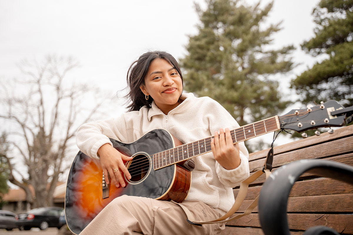 A student sits on a bench and plays the guitar